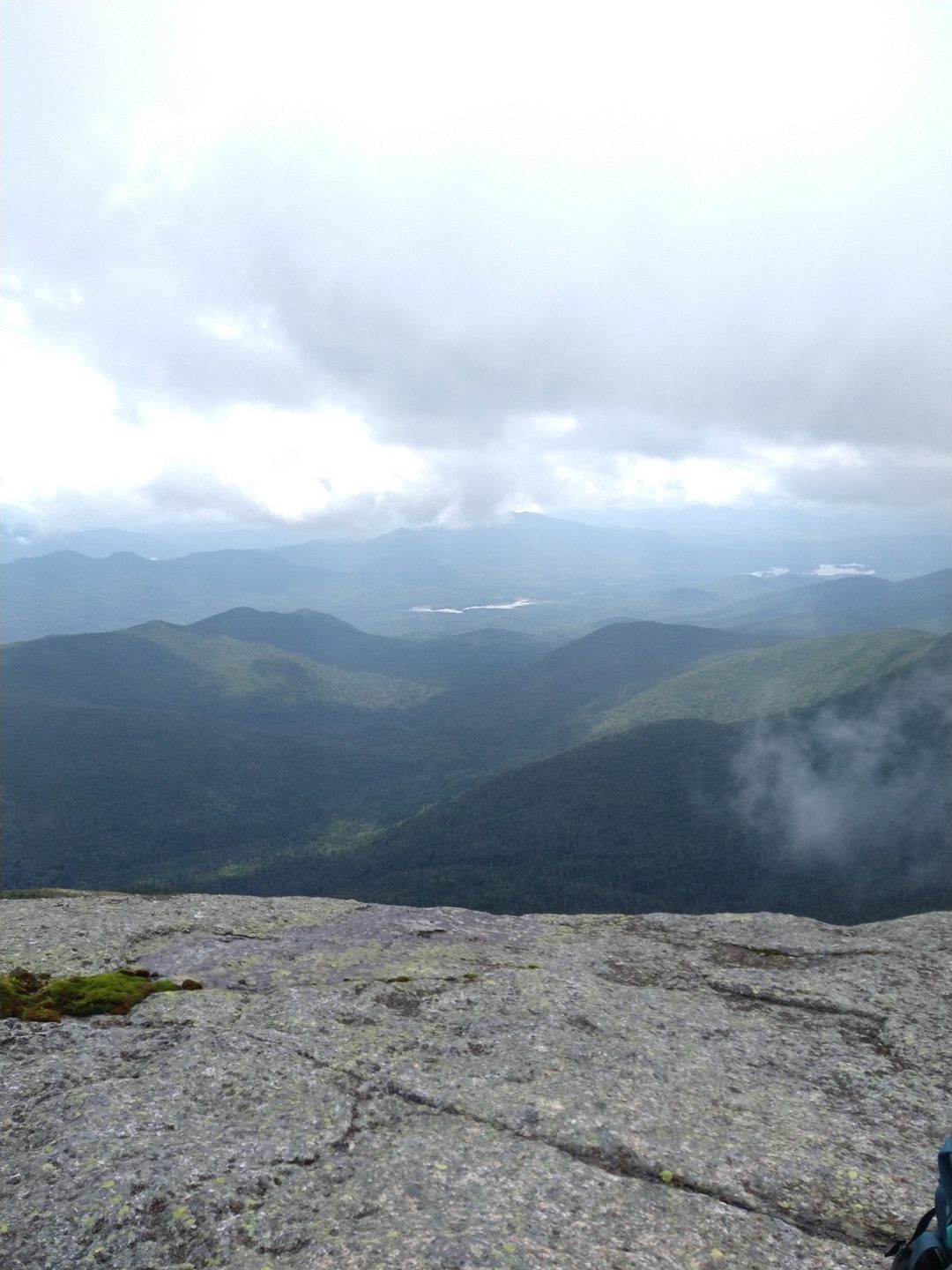 Layered mountain ridges under clouds, seen from a bare rocky summit