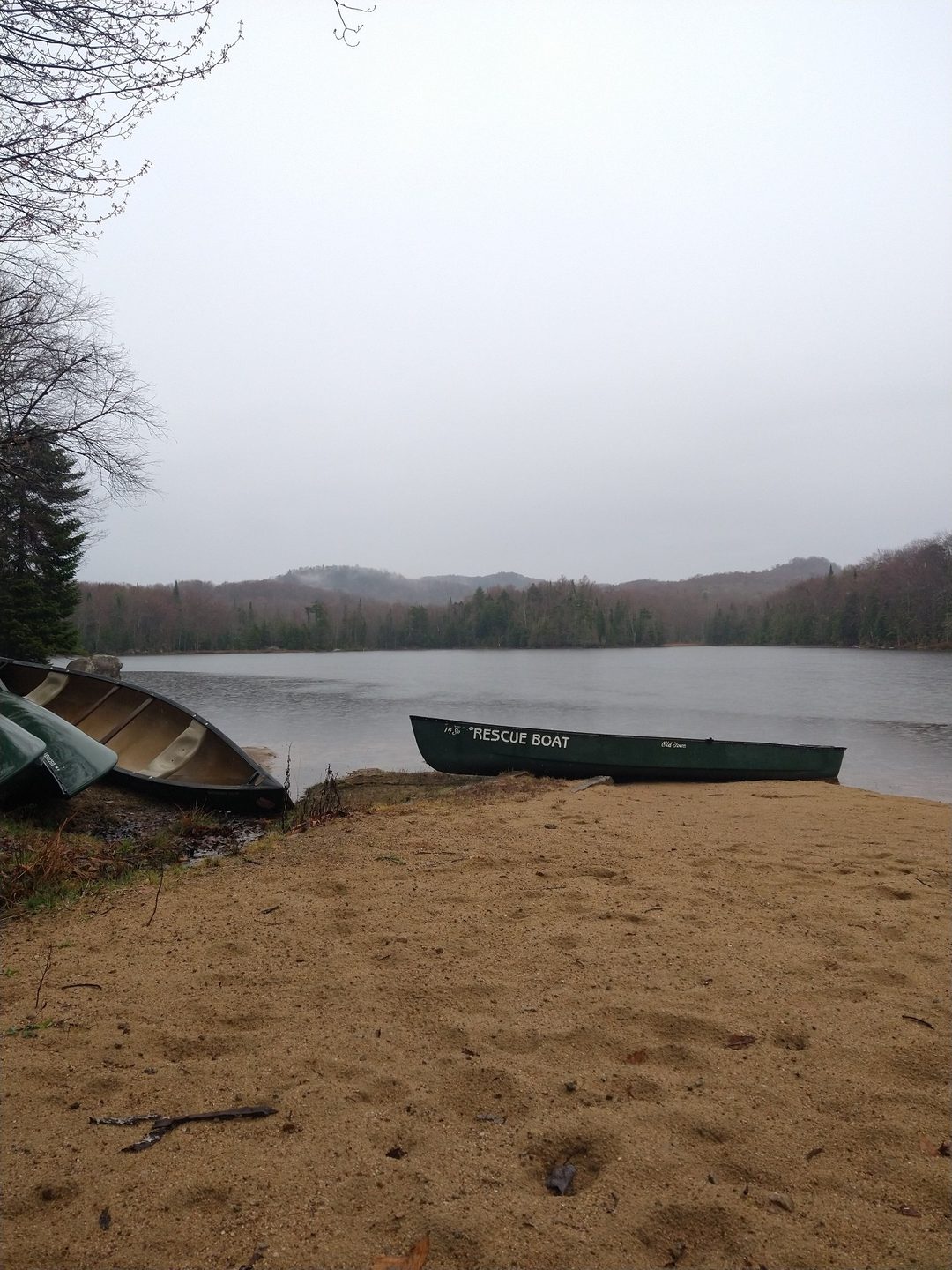 Canoes pulled up on a sandy shore beside a misty lake